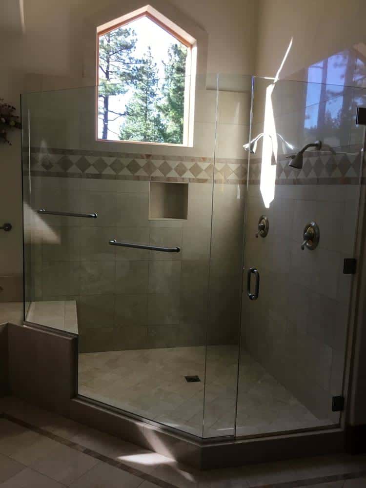 07-1-1 A modern glass-enclosed shower with a built-in bench, tiled walls, and an arched window showing trees.