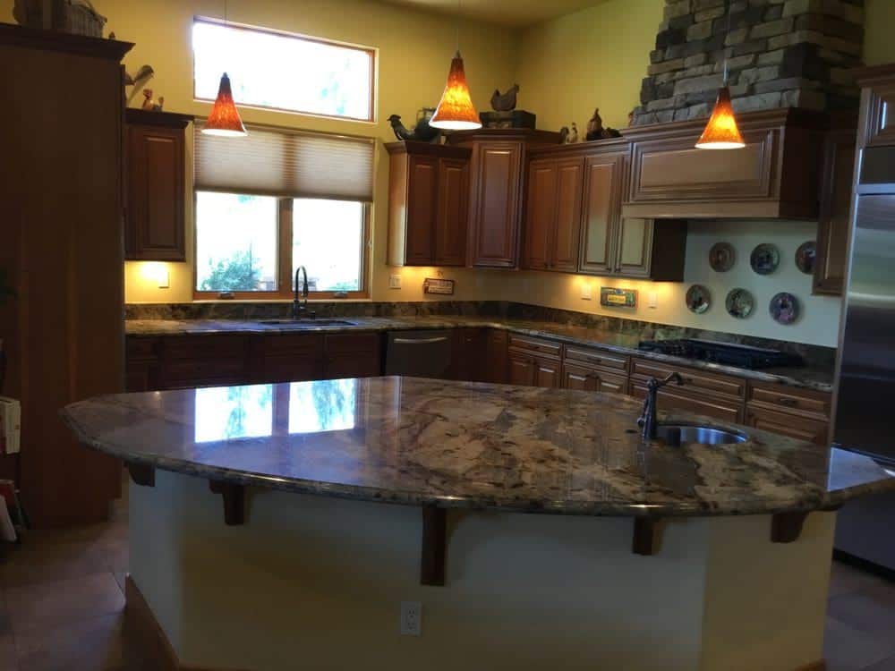 08-1-1 A spacious kitchen features a large granite island, dark wood cabinets, and a stone-faced range hood.