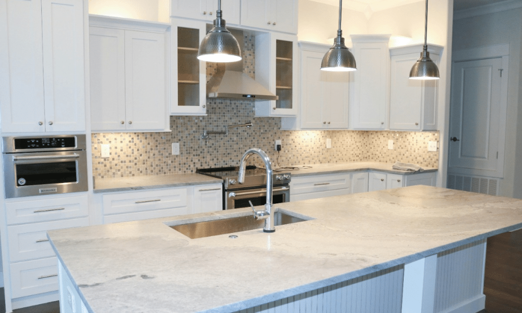 A modern kitchen with white cabinets, light gray marble countertops, and a tiled backsplash.