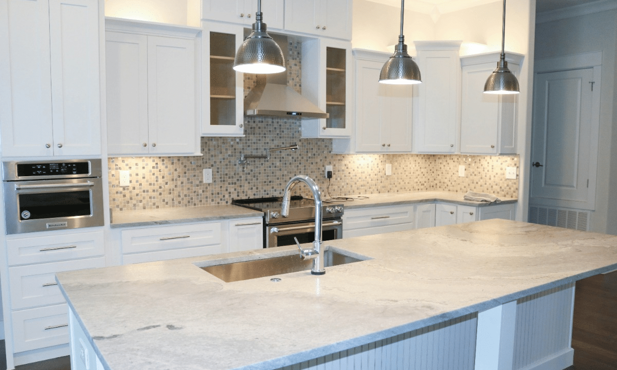 A modern kitchen with white cabinets, light gray marble countertops, and a tiled backsplash.