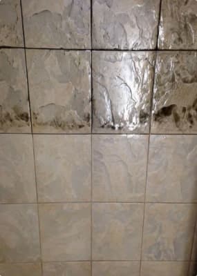Light-colored square tiles with dark grime and mold along the bottom edge of the top row of tiles.