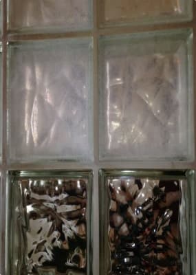 A wall of square glass blocks, some clear and some with a rippled, reflective texture.