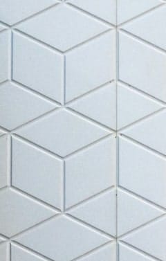 A white geometric wall with a repeating pattern of embossed rhombus and cube shapes.