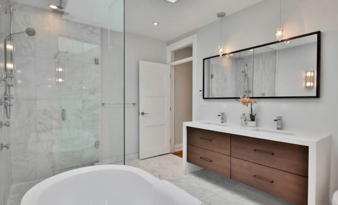 A modern bathroom features a glass shower, a white freestanding tub, and a double vanity with dark wood drawers.
