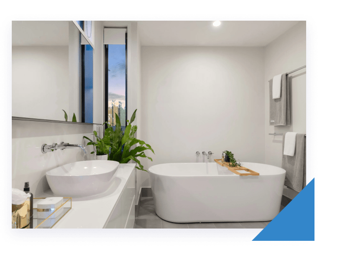 A modern bathroom with a white oval bathtub, a sink, a large mirror, and a window with green plants.