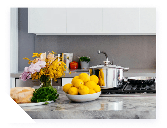 A modern kitchen with white cabinets, a granite countertop, a vase of flowers, lemons, and a pot on the stove.