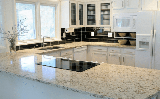 A modern kitchen with white cabinets, light granite countertops, a black subway tile backsplash, and stainless steel appliances.
