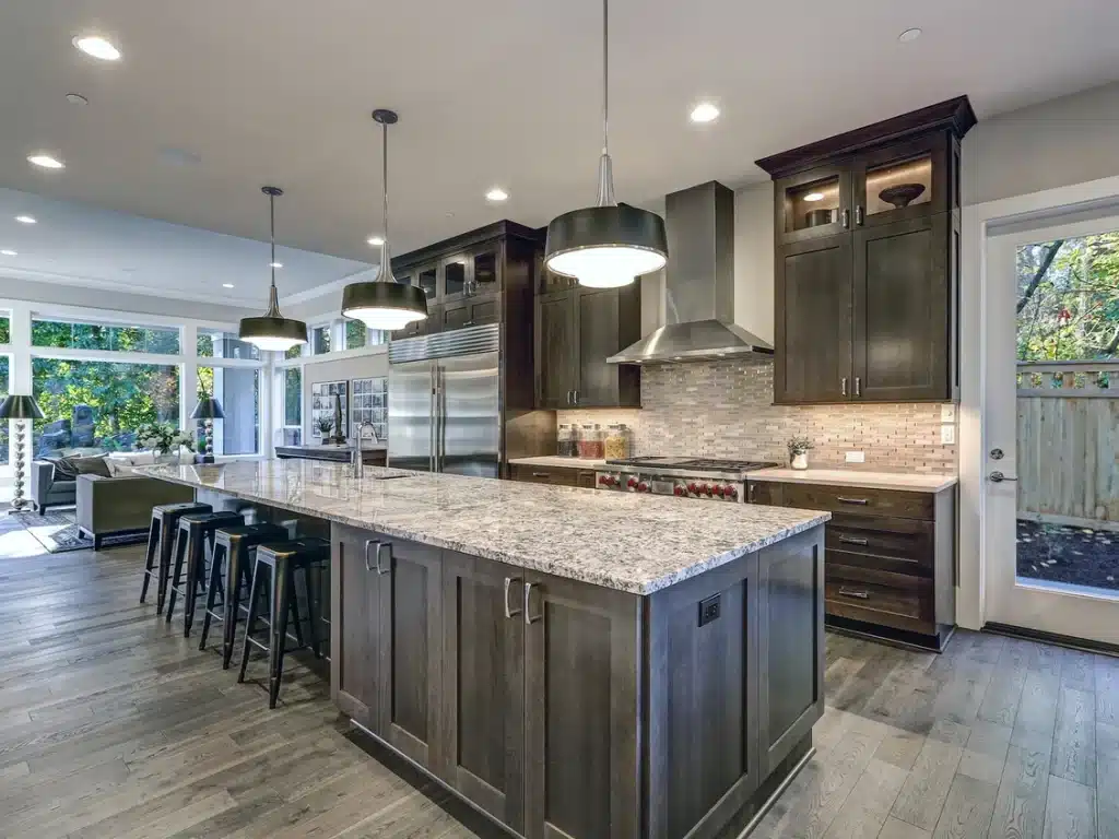 A modern kitchen with dark wood cabinets, a large granite island with stools, and stainless steel appliances.