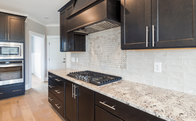 A modern kitchen features dark wood cabinets, a granite countertop, a gas stove, and white subway tile backsplash.