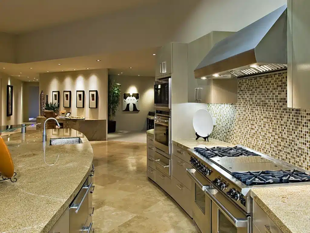 A modern kitchen features a curved granite island, stainless steel appliances, and a mosaic tile backsplash.