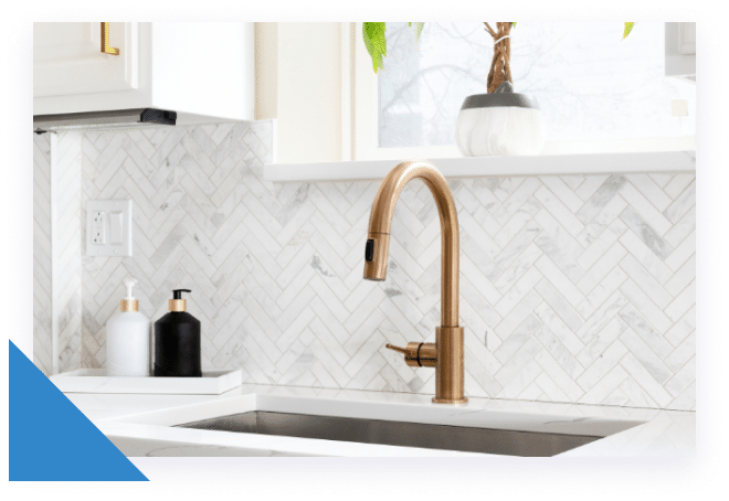 A modern kitchen sink with a gold faucet, white herringbone tile backsplash, and two soap dispensers.