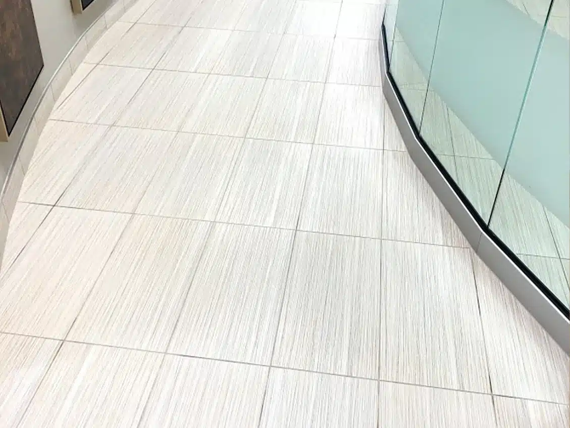 A light-colored tiled floor with a subtle striped pattern curves left, meeting a glass and metal railing on the right.