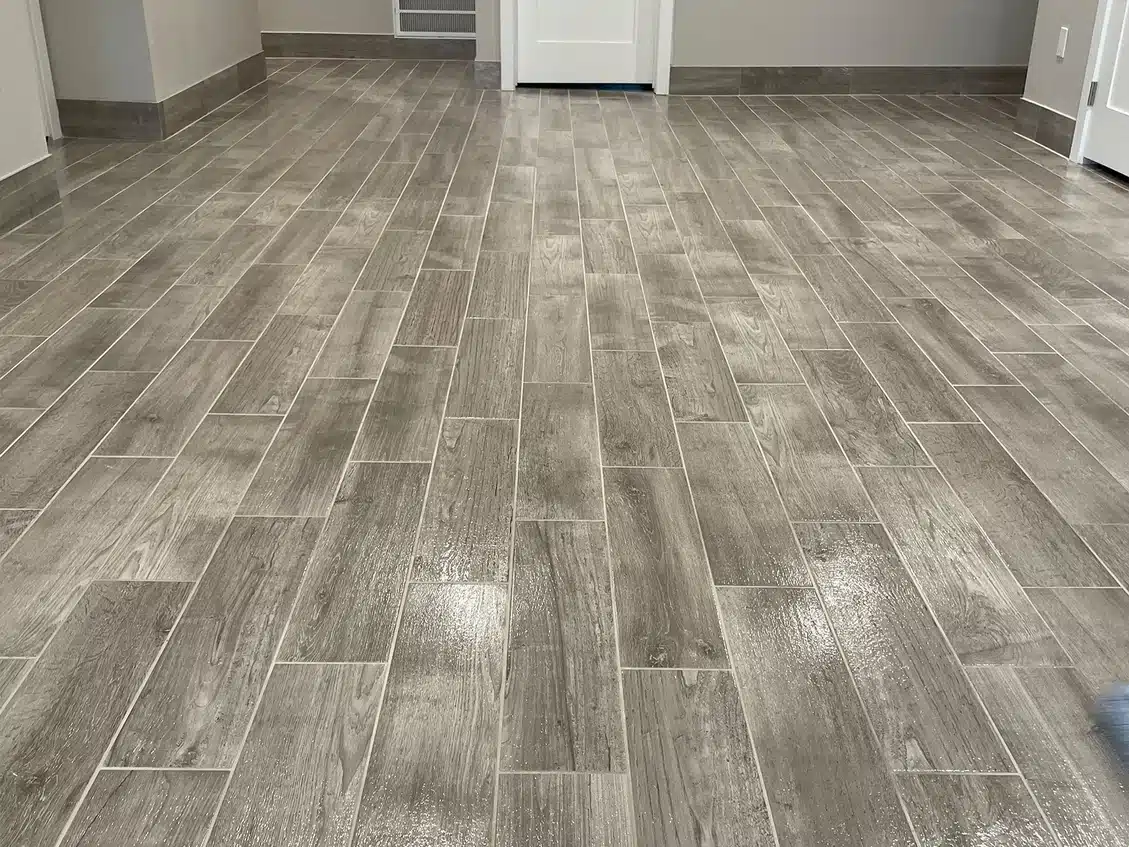 A clean, gray tiled floor with a wood grain pattern extends from the foreground to two white doors in the background.