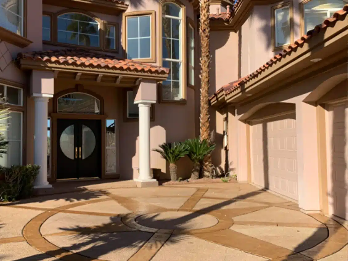 A large, light pink house with a brown tile roof, dark double doors, and a decorative circular driveway.